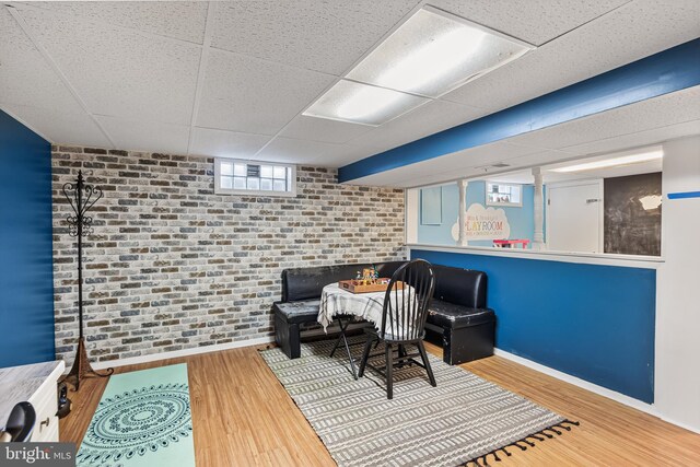 sitting room featuring baseboards, a paneled ceiling, wood finished floors, and brick wall