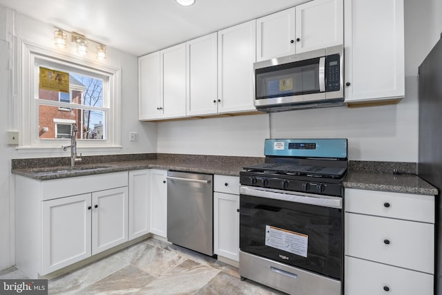 kitchen featuring appliances with stainless steel finishes, dark stone counters, white cabinets, and a sink