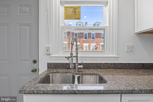 kitchen with dark stone counters, a sink, and white cabinets