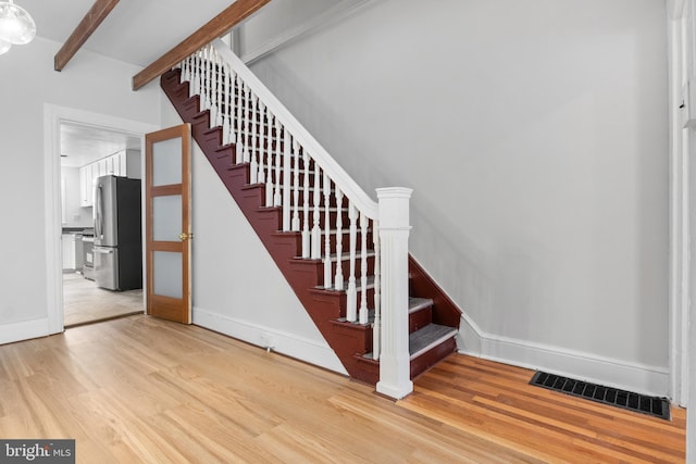 stairway with beam ceiling, wood finished floors, visible vents, and baseboards