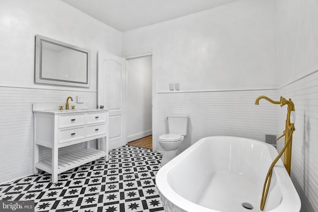 bathroom featuring wainscoting, toilet, a soaking tub, tile patterned floors, and vanity