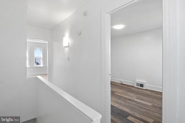 corridor with dark wood-style flooring, visible vents, baseboards, and an upstairs landing