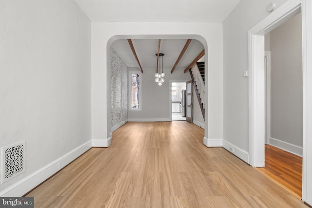 interior space featuring light wood finished floors, baseboards, visible vents, and beamed ceiling