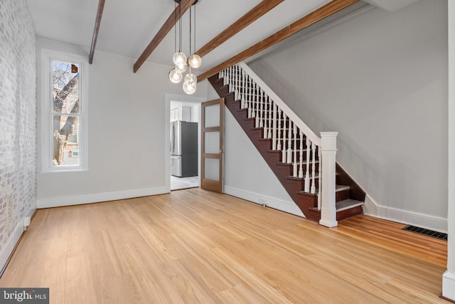 unfurnished living room featuring baseboards, visible vents, wood finished floors, beamed ceiling, and stairs