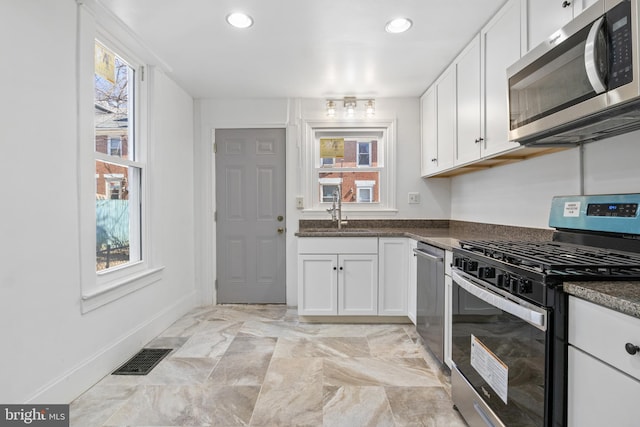 kitchen with stainless steel appliances, a sink, visible vents, a wealth of natural light, and dark countertops