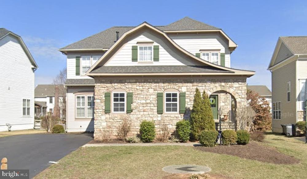 view of front of property featuring stone siding, a front lawn, and roof with shingles