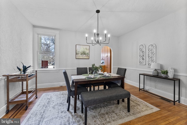 dining space featuring baseboards, arched walkways, wood finished floors, and a chandelier