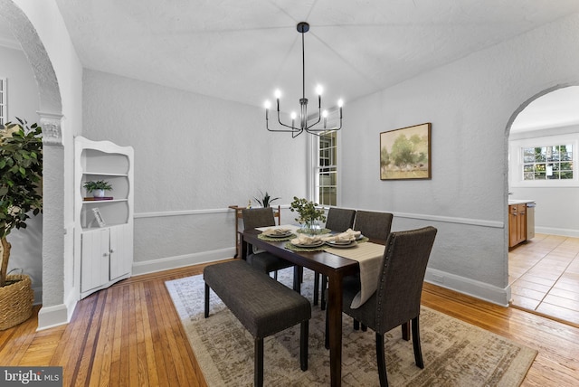 dining space with light wood finished floors, baseboards, a chandelier, a textured wall, and arched walkways