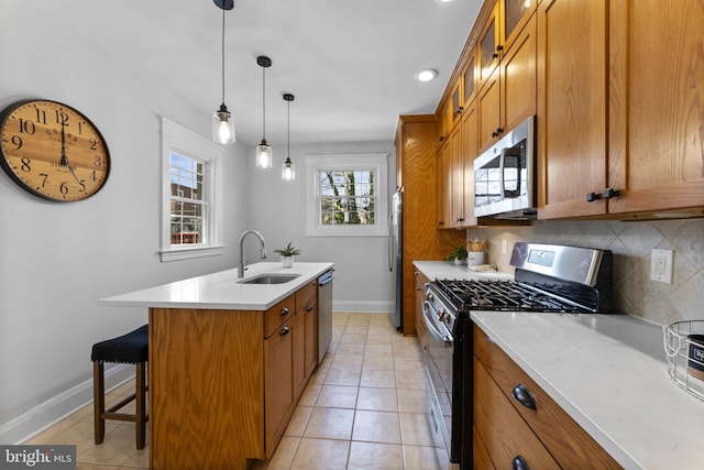 kitchen with backsplash, a center island with sink, brown cabinetry, stainless steel appliances, and a sink