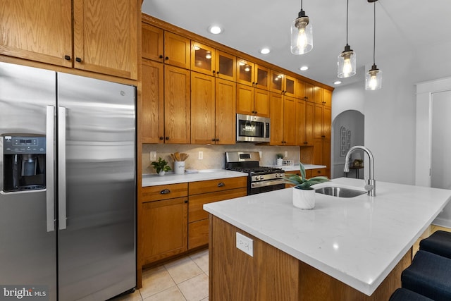 kitchen with light tile patterned floors, brown cabinetry, a sink, stainless steel appliances, and tasteful backsplash