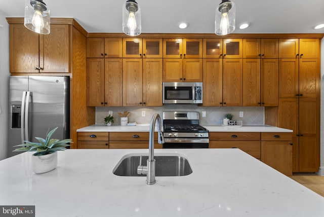 kitchen featuring a sink, stainless steel appliances, brown cabinetry, and hanging light fixtures