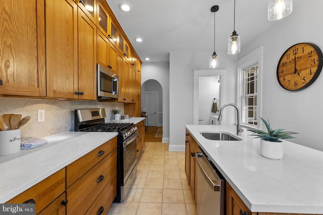 kitchen featuring brown cabinetry, arched walkways, a sink, appliances with stainless steel finishes, and tasteful backsplash