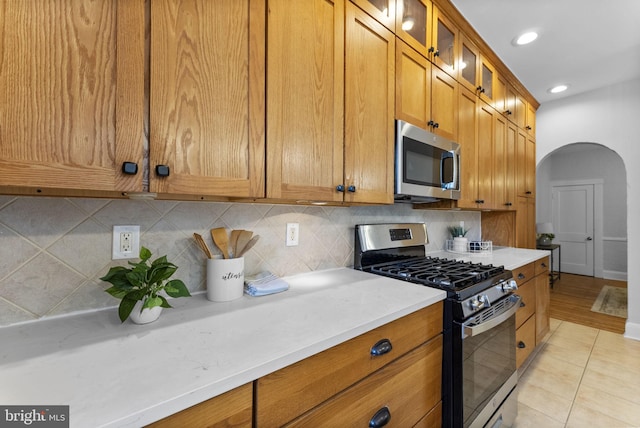 kitchen with backsplash, light countertops, brown cabinets, arched walkways, and stainless steel appliances