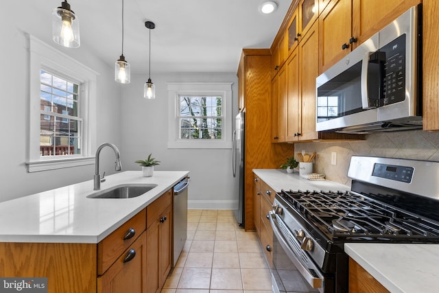 kitchen featuring pendant lighting, a sink, backsplash, appliances with stainless steel finishes, and brown cabinetry