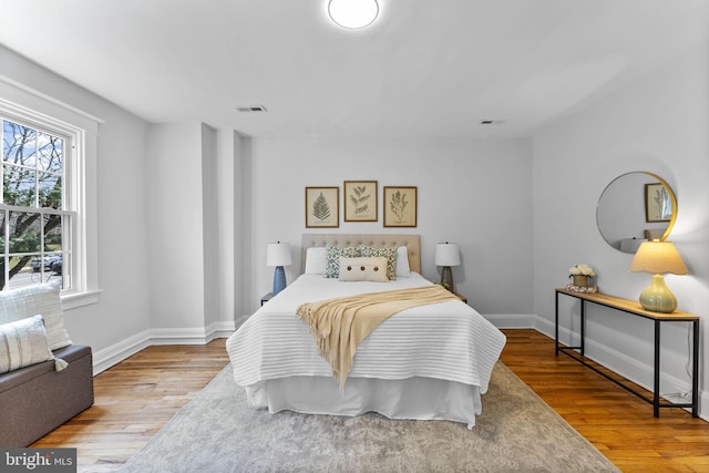 bedroom with wood finished floors, visible vents, and baseboards