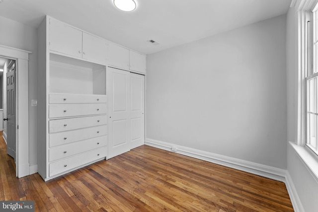 unfurnished bedroom featuring a closet, visible vents, dark wood-type flooring, and baseboards