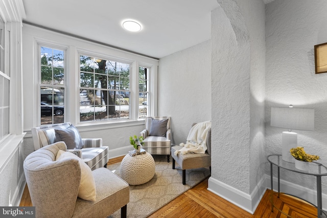 sitting room featuring baseboards, a textured wall, and wood finished floors