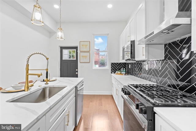 kitchen with decorative backsplash, wall chimney exhaust hood, stainless steel appliances, light wood-style floors, and a sink