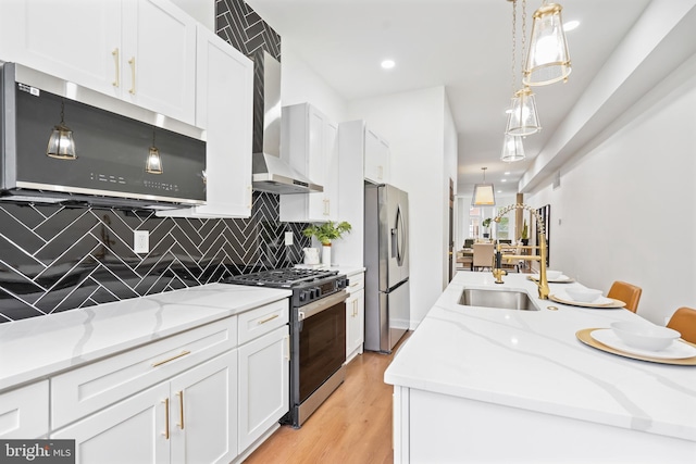 kitchen with light wood-style flooring, appliances with stainless steel finishes, white cabinetry, a sink, and wall chimney exhaust hood