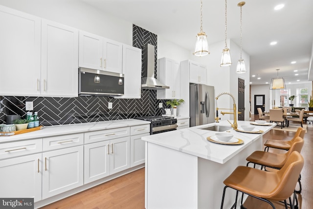 kitchen featuring a kitchen island with sink, stainless steel appliances, a sink, white cabinetry, and light wood finished floors