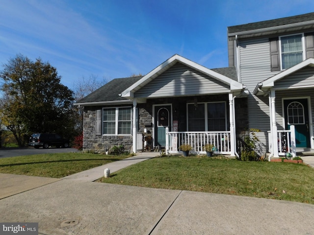 view of front of house with stone siding, roof with shingles, a porch, and a front yard