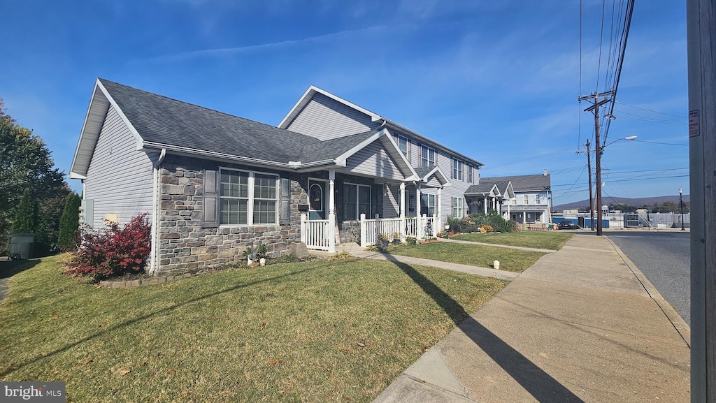 view of front of home with a shingled roof, stone siding, and a front lawn