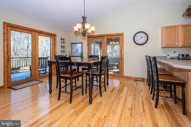 dining space with light wood-style floors, a wealth of natural light, vaulted ceiling, and an inviting chandelier