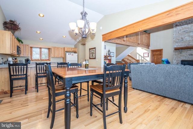 dining room with lofted ceiling, an inviting chandelier, light wood-style flooring, and a stone fireplace