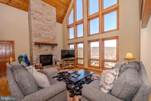 living room with high vaulted ceiling, wood ceiling, a stone fireplace, and wood finished floors