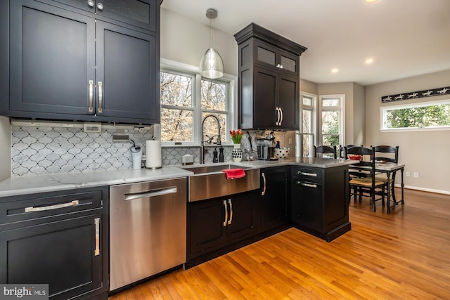 kitchen with light wood-type flooring, a sink, backsplash, stainless steel dishwasher, and hanging light fixtures