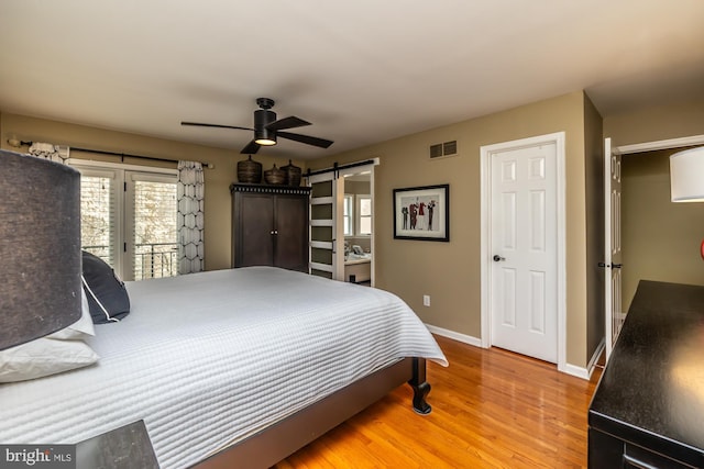 bedroom featuring wood finished floors, baseboards, visible vents, a barn door, and access to outside