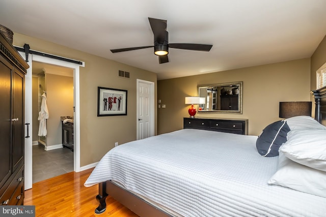 bedroom with baseboards, visible vents, light wood finished floors, ceiling fan, and a barn door