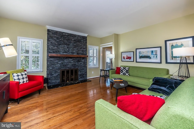 living area with baseboards, a stone fireplace, and wood finished floors