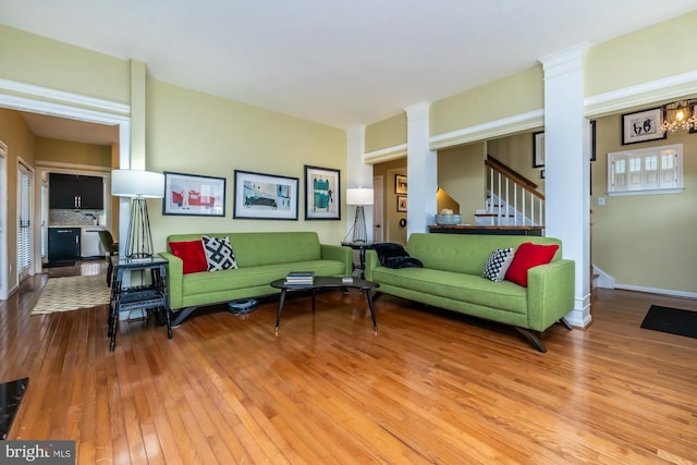 living area with decorative columns, wood-type flooring, baseboards, and stairway