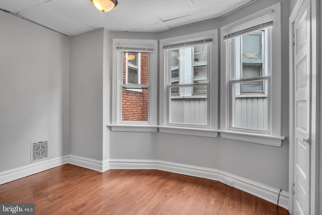 unfurnished room featuring visible vents, a drop ceiling, baseboards, and wood finished floors