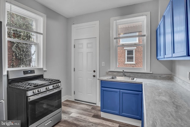 kitchen with stainless steel gas range oven, blue cabinets, wood finished floors, and a sink