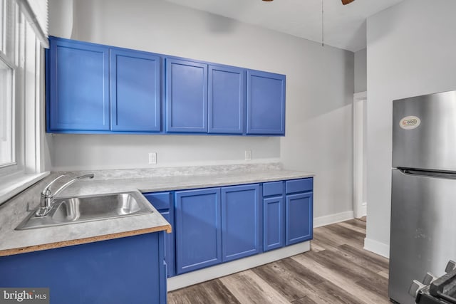 kitchen with a sink, blue cabinetry, wood finished floors, freestanding refrigerator, and light countertops