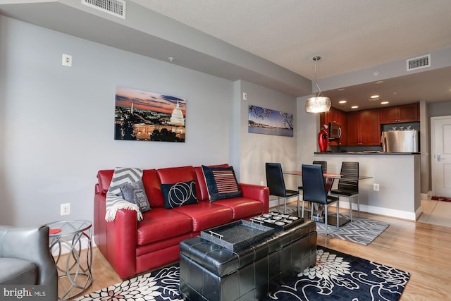 living area with light wood-type flooring, visible vents, and baseboards