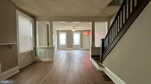 entrance foyer featuring a textured ceiling, ceiling fan, wood finished floors, stairway, and ornate columns