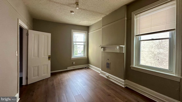 empty room with a textured ceiling, dark wood-style flooring, visible vents, and baseboards