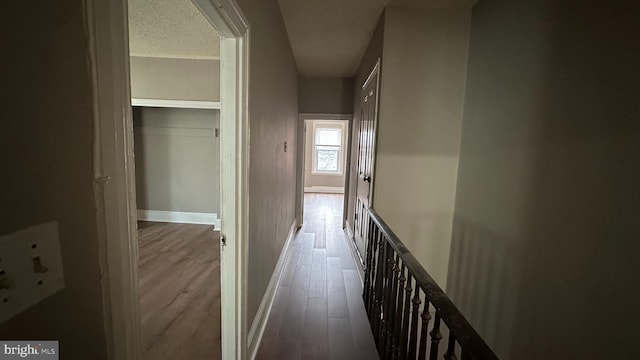 hallway with a textured ceiling, wood finished floors, and baseboards