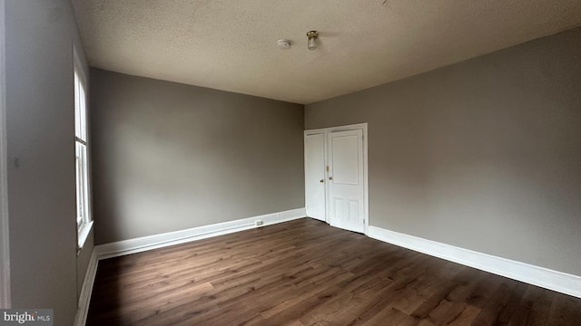 unfurnished room with a textured ceiling, dark wood finished floors, and baseboards