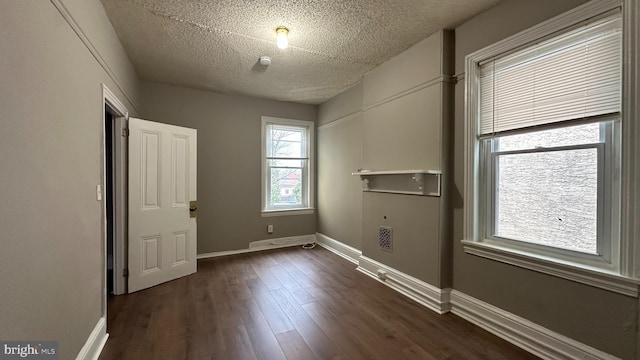 empty room with dark wood-style floors, a textured ceiling, and baseboards