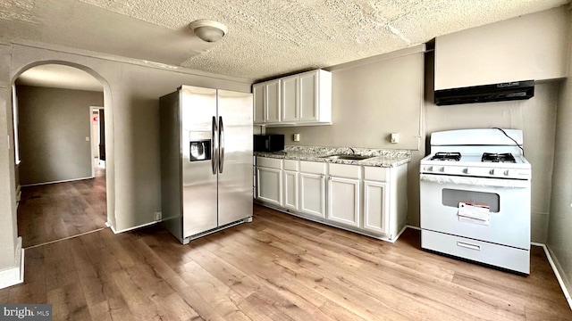 kitchen with arched walkways, under cabinet range hood, light wood-type flooring, white gas range, and stainless steel fridge