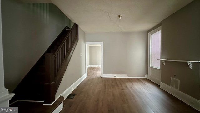 unfurnished dining area with stairway, visible vents, baseboards, and dark wood-style flooring