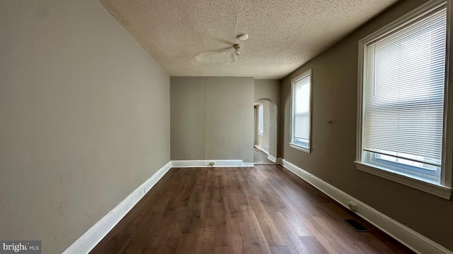 spare room featuring arched walkways, dark wood-style flooring, visible vents, and baseboards