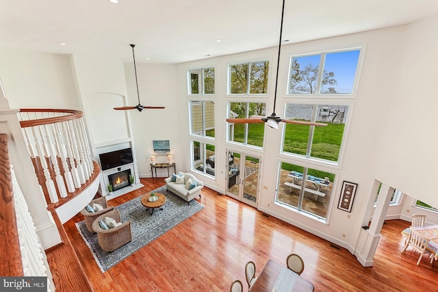 living area with baseboards, a ceiling fan, a towering ceiling, a fireplace with flush hearth, and wood finished floors