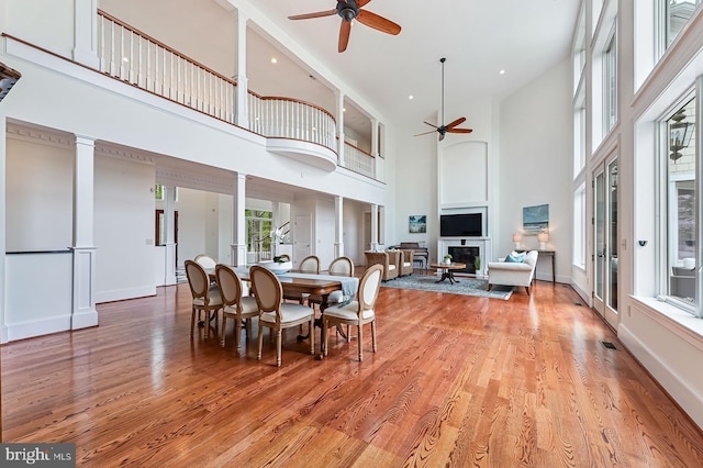 dining area featuring light wood-style floors, a fireplace, decorative columns, and ceiling fan