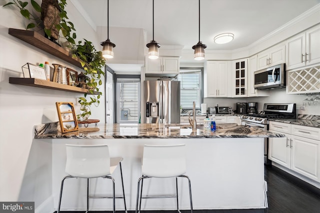 kitchen with white cabinetry, appliances with stainless steel finishes, dark stone counters, and a peninsula