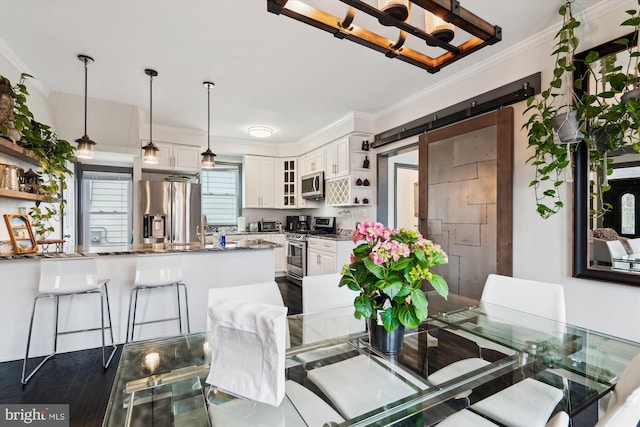 dining room featuring a barn door, a notable chandelier, dark wood-type flooring, and ornamental molding